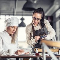 Foto af en kvindelig kok og en servitrice med en iPad og en lommeregner.