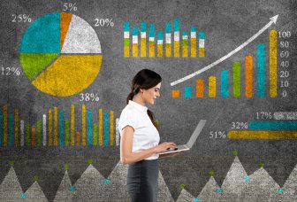 Foto: kvinde stående med en pc foran en væg med grafer og tal.