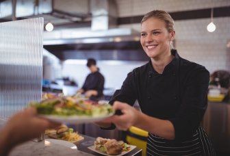 Foto af en smilende dame i en kantine, der serverer mad.