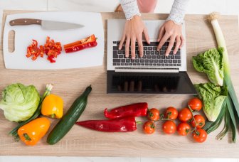 Illustrationsfoto af en person, der arbejder på en computer med grøntsager på et bord.