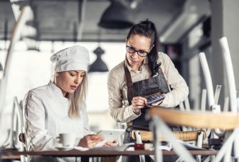 Foto af en kvindelig kok og en servitrice med en iPad og en lommeregner.