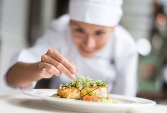 Illustrationsfoto af en kok, der tilføjer den sidste ingrediens til en ret.
